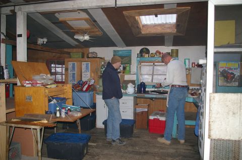 1986 Ford Bronco - Two men are inside a rustic cabin, one preparing food at a counter while the other stands nearby.
