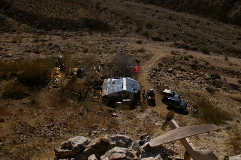 1986 Ford Bronco - Multiple vehicles are parked near a remote structure in a dry, hilly terrain.