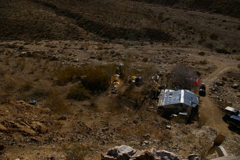 1986 Ford Bronco - Two SUVs are parked on a dirt road next to a small dwelling in a dry, rocky desert environment.