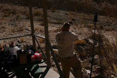 1986 Ford Bronco - A person takes aim with a rifle from a covered structure in a dry, rocky environment.