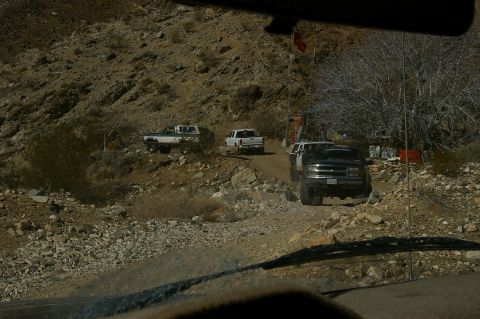1986 Ford Bronco - Several trucks and SUVs traverse a , mountainous terrain on a sunny day.