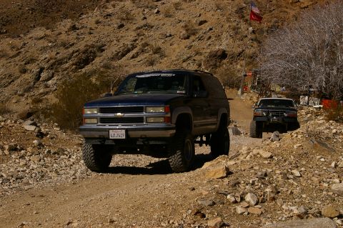 1986 Ford Bronco - Two SUVs navigate a rough dirt path in a desert landscape.