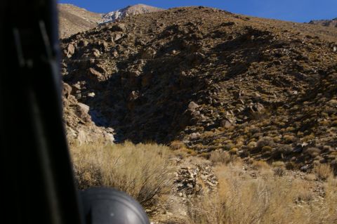 1986 Ford Bronco - Driving through a dry, mountainous terrain with scrub brush and rocks under a bright blue sky.