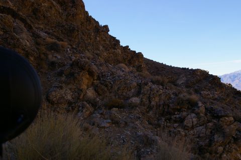 1986 Ford Bronco - A black tire is partially visible in the foreground of a rocky, arid landscape under a clear blue sky.