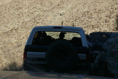 1986 Ford Bronco - A 1986 Ford Bronco navigates a rocky terrain, its spare tire prominently displayed on the rear door.