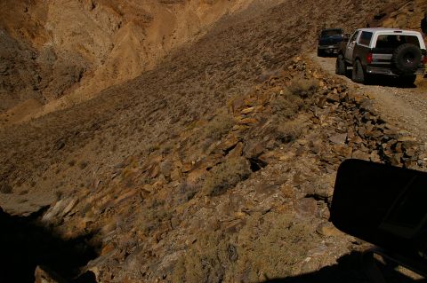 1986 Ford Bronco - Two SUVs navigate a narrow dirt road on a steep mountainside, with the lead vehicle a 1986 Ford Bronco.