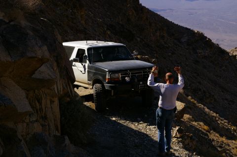 1986 Ford Bronco - A man signals to a Ford Bronco navigating a precarious mountain path.