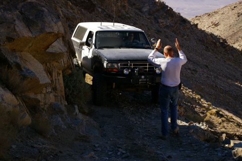1986 Ford Bronco - A black and white Ford Bronco navigates a rocky, off-road path, with a person standing nearby.