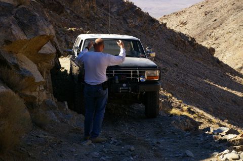 1986 Ford Bronco - Ford Bronco driving on a rough, off-road path through a mountainous desert landscape.