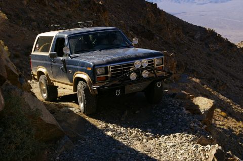 1986 Ford Bronco - Ford Bronco navigates a challenging off-road path in a mountainous desert landscape.