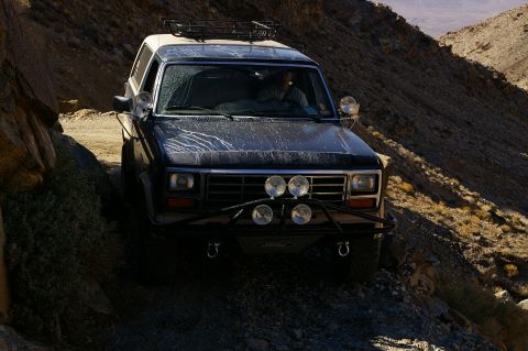 1986 Ford Bronco - This Ford Bronco is navigating a narrow, rocky trail with steep hillsides on either side.