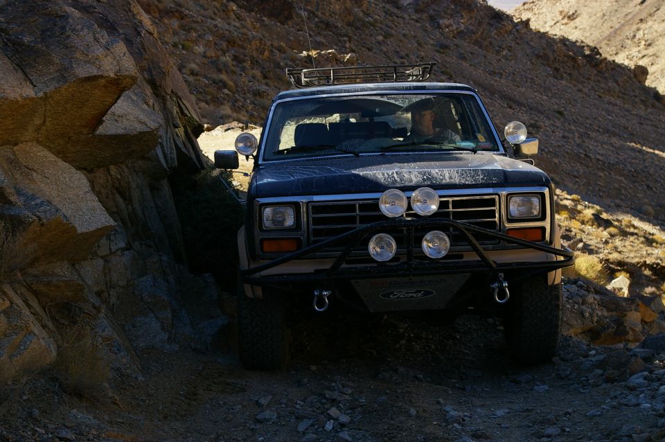 1986 Ford Bronco navigating a narrow, rocky off-road path with a driver visible