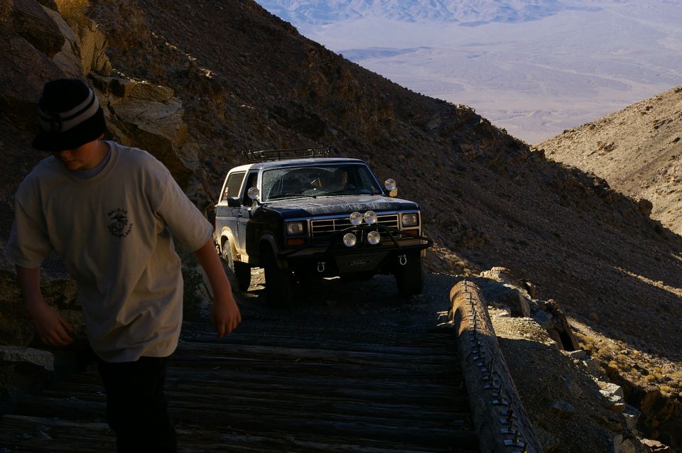 Ford Bronco driving on a dirt road in a mountainous area. Person in foreground