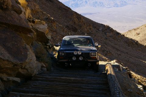 1986 Ford Bronco - A dark SUV navigates a treacherous wooden path on a steep mountain incline.