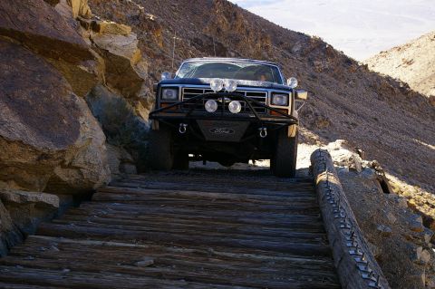 1986 Ford Bronco - A dark blue 1986 Ford Bronco navigates a precarious wooden bridge in a rocky, mountainous terrain.