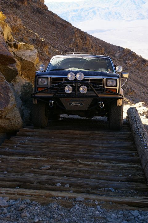 1986 Ford Bronco - 1986 Ford Bronco navigates a rough wooden bridge in a desert landscape.
