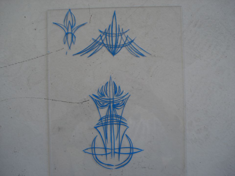 Blue pinstripe art on clear plastic sheet, showing three designs including a flame-like shape and a stylized face