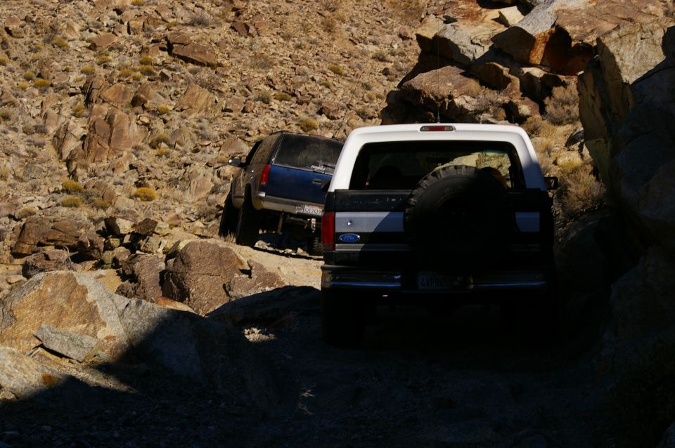 White Ford Bronco with spare tire on rear, driving on rocky terrain