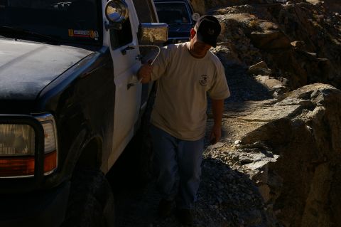 1986 Ford Bronco - A man exits a two-tone SUV navigating a rough, rocky terrain.