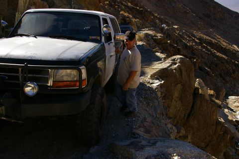 1986 Ford Bronco - Ford F-Series truck navigates a steep, rocky mountain road with another vehicle visible in the distance.