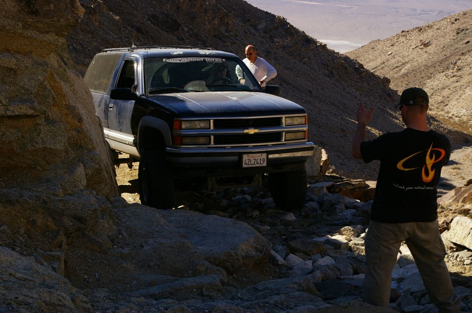Black Chevrolet Suburban driving on a rocky trail, driver waves