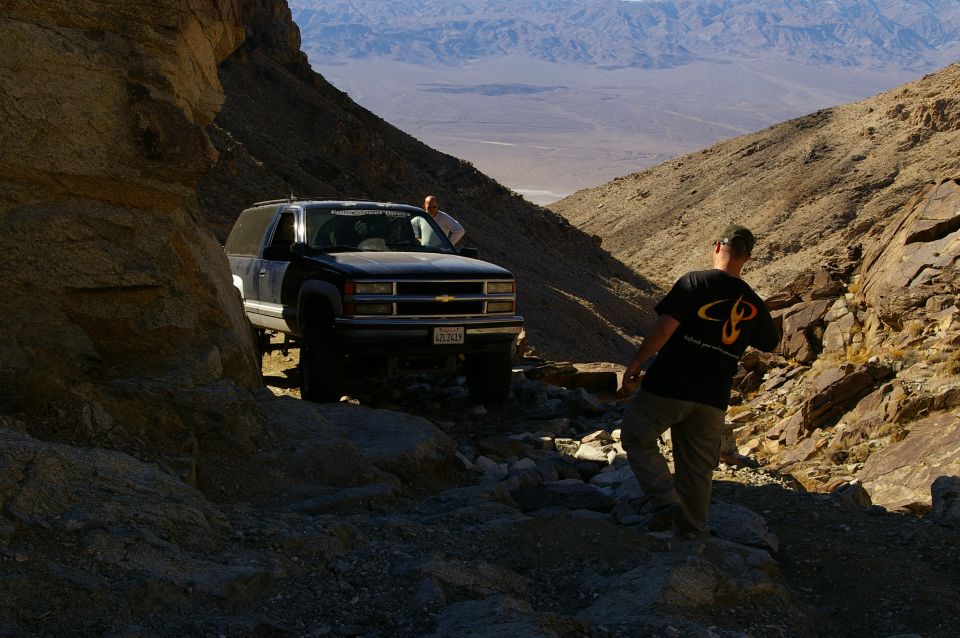 Black Chevrolet Suburban navigating a narrow, rocky mountain trail with two people visible