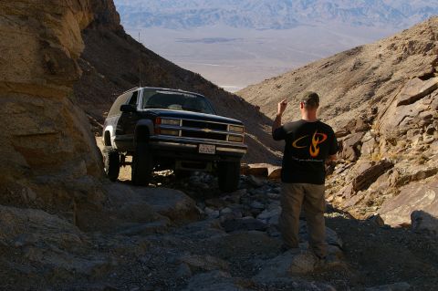 1986 Ford Bronco - A person directs a lifted black SUV on a rough, mountainous terrain.