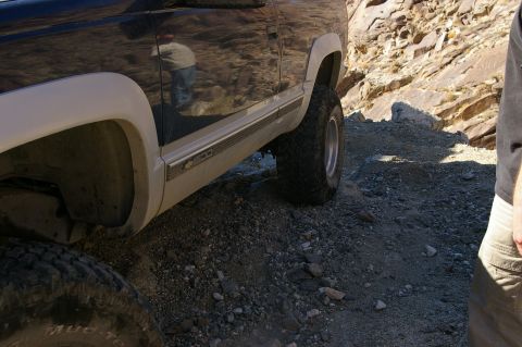 1986 Ford Bronco - A dark SUV with white fender flares navigates a rocky, off-road path.