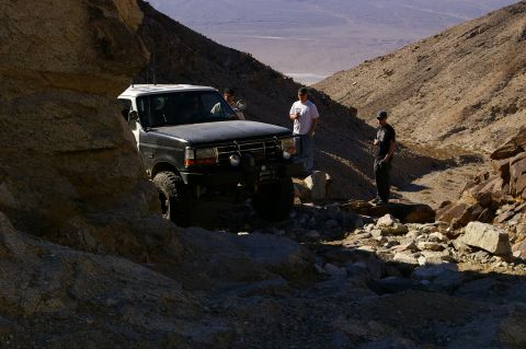 1986 Ford Bronco - A group of people stand near a lifted Ford F-series truck navigating a rocky desert trail.
