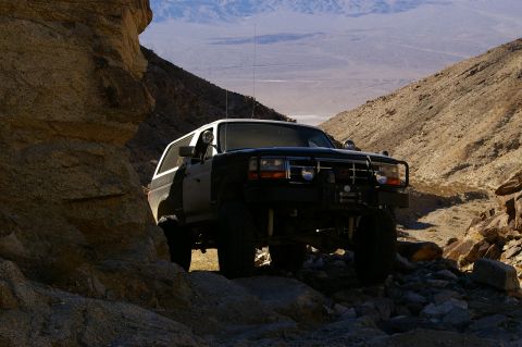 1986 Ford Bronco - A Ford Bronco navigates a narrow, rocky canyon in a desert landscape.