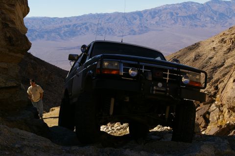 1986 Ford Bronco - Ford Bronco tackling a rough off-road path in a desert canyon landscape.