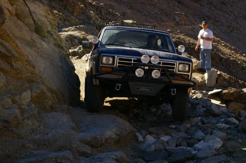 1986 Ford Bronco - Ford Bronco tackling a challenging off-road path in a rocky, desert-like environment.