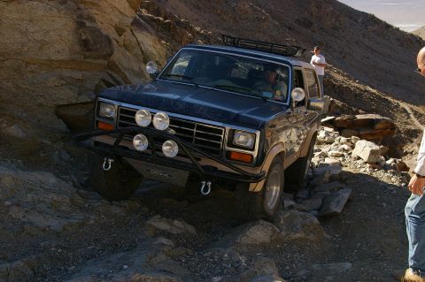 1986 Ford Bronco - Ford Bronco tackling a challenging off-road path in a desert landscape.