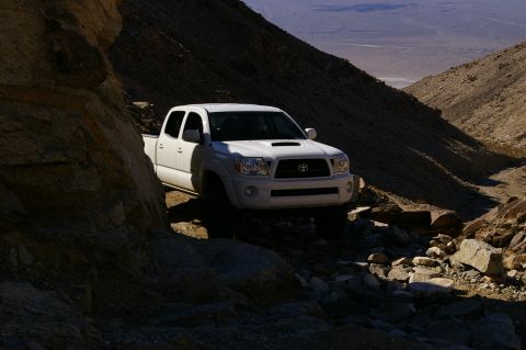 1986 Ford Bronco - Toyota Tacoma navigates a rough, rocky path through a desert canyon.