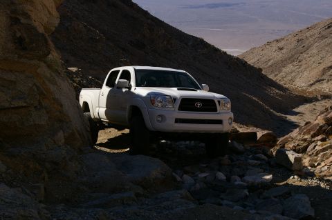 1986 Ford Bronco - A white Toyota Tacoma navigates a challenging off-road path through a rocky canyon.