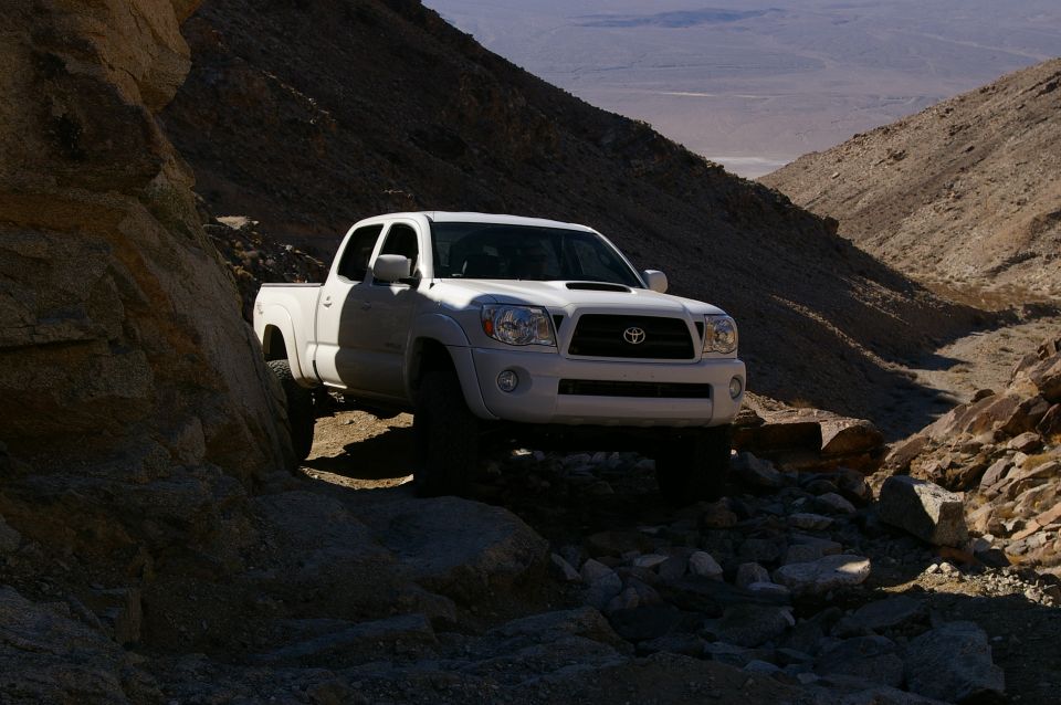 White Toyota Tacoma pickup truck driving on a rocky, narrow mountain trail