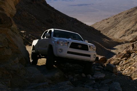 1986 Ford Bronco - A white Toyota Tacoma navigates a challenging, rocky trail in a desert canyon.