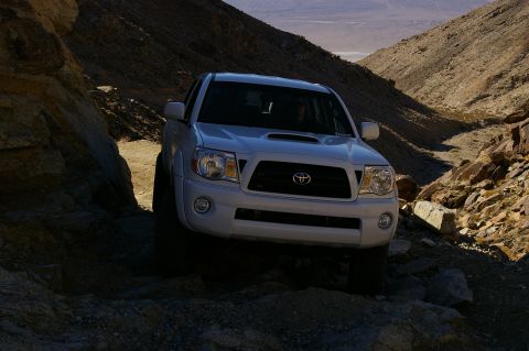 1986 Ford Bronco - White Toyota Tacoma navigates a desert path, highlighting its off-road capability.