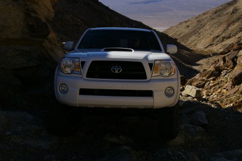 1986 Ford Bronco - White Toyota Tacoma truck navigates a narrow, rocky path in a desert canyon.