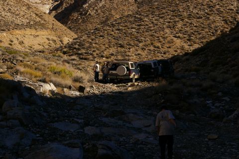 1986 Ford Bronco - Two SUVs are stopped on a rocky, arid trail in a canyon, with people standing near the vehicles.