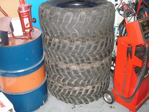 1994 Ford Bronco - Four large off-road tires are stacked next to a barrel and a red automotive diagnostic machine.