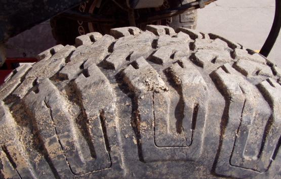 Close-up of a dirty, off-road tire tread with large, blocky lugs