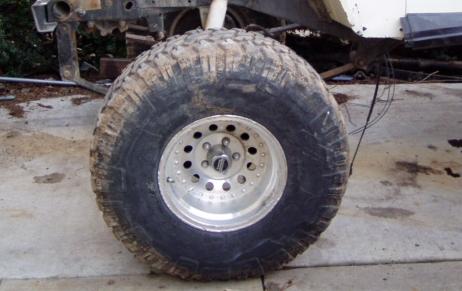 1991 Ford Bronco - A close-up view of a large, mud-caked off-road tire mounted on a silver rim.