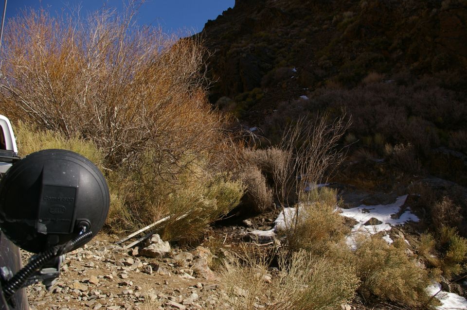 Black auxiliary light mounted on the side of a vehicle, with dry brush and rocky terrain in the background