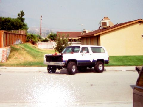 1996 Ford Bronco - A white and blue SUV is parked on the side of the road with its front grille missing.