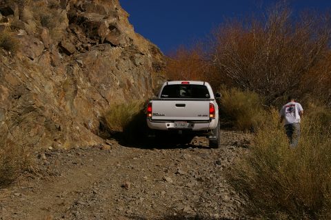 1986 Ford Bronco - A white Toyota pickup truck navigates a rough, rocky terrain under a clear blue sky.