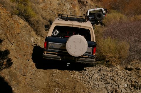1986 Ford Bronco - Two Ford Broncos navigate a , rocky trail in a dry, brushy landscape.
