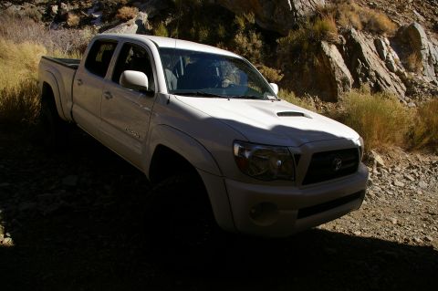1986 Ford Bronco - A white Toyota Tacoma pickup truck is parked on a rough, rocky terrain with sparse vegetation.