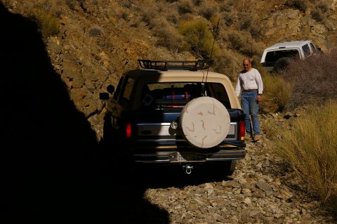 1986 Ford Bronco - Two SUVs navigate a rough, rocky trail in a desert landscape.