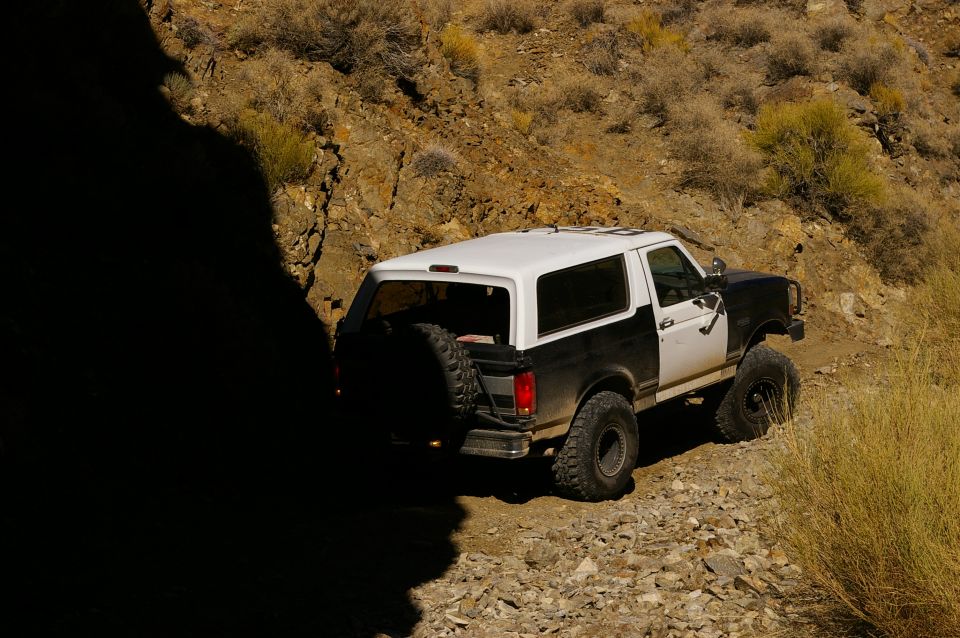 Two-tone black and white Ford Bronco with a spare tire mounted on the rear, driving on a rocky dirt road